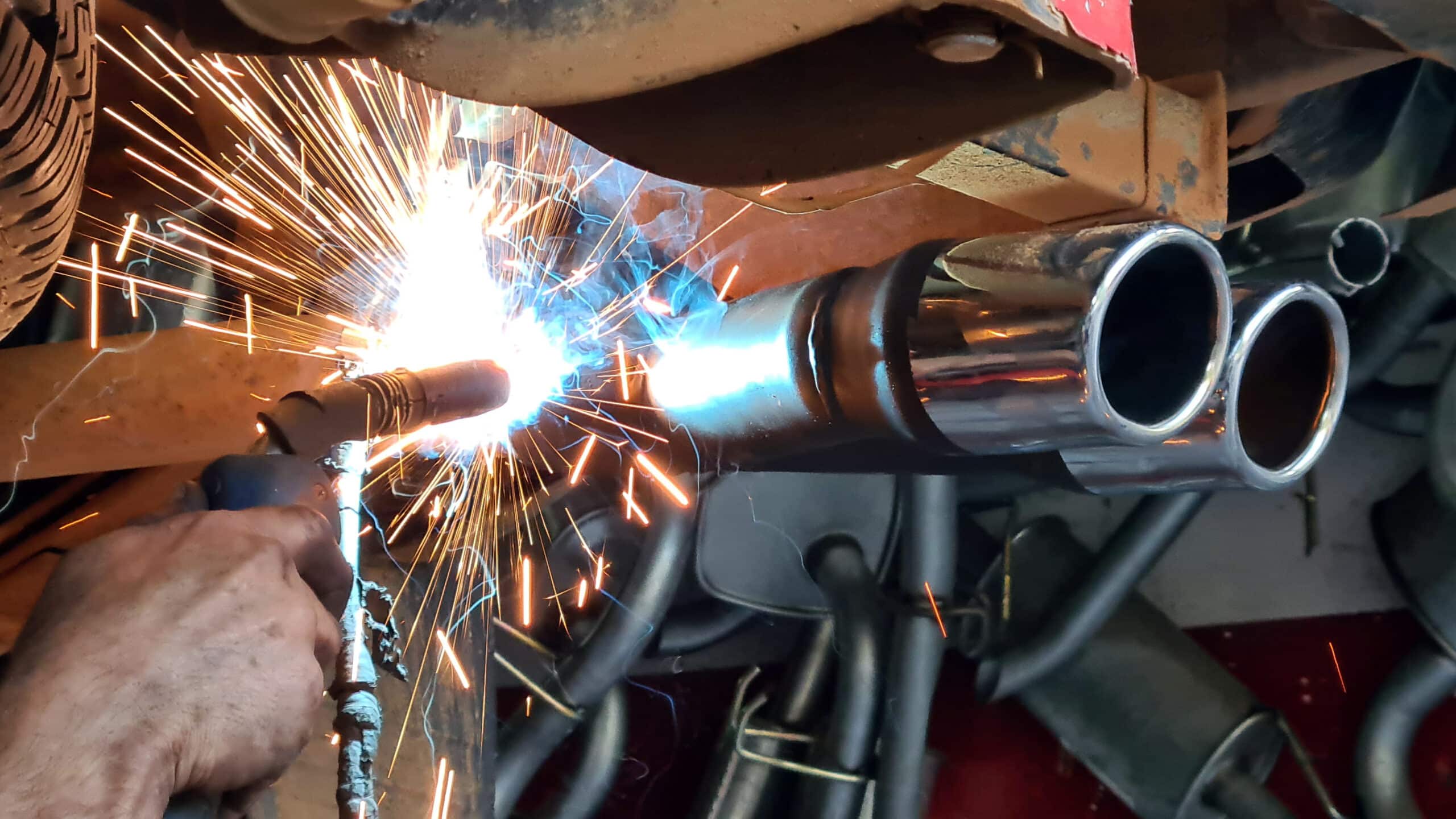 Soudure d'un système d'échappement de voiture, étincelles brillantes et fumée bleue d'un arc électrique sur un pot chromé.